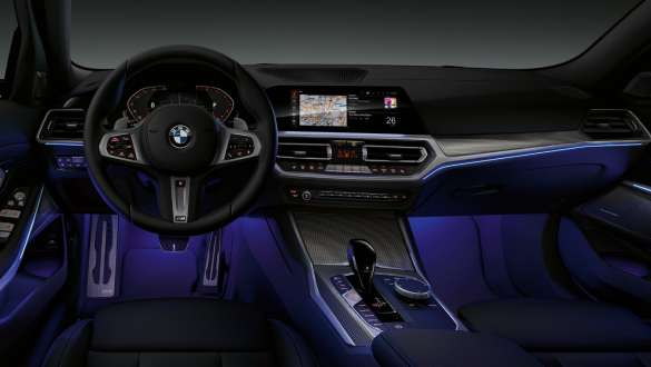 BMW 3 серии Седан (G20), освещение Ambient Вид спереди на кокпит водителя седана BMW 3 серии (G20) с голубой подсветкой пространства для ног от Ambient.