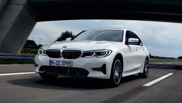 Плагин-гибрид BMW 3 серии Седан 2021 G20, вид спереди в три четверти в движении Плагин-гибрид BMW 3 серии Седан 2021 G20, вид спереди в три четверти в движении по улице
