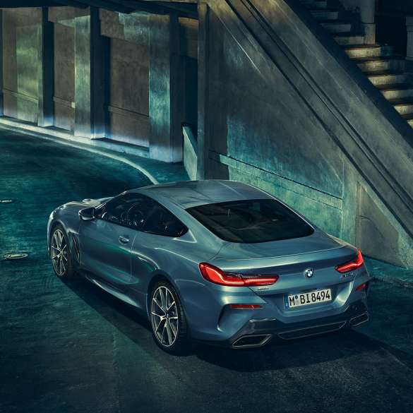 BMW M850i xDrive Coupé, вид сзади с поворотом в три четверти слева. BMW M850i xDrive Coupé в Barcelona Blue металлик, вид сзади с поворотом в три четверти слева, стоит ночью.