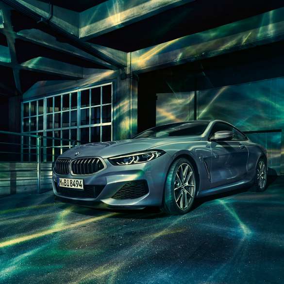 BMW M850i xDrive Coupé, вид спереди с поворотом в три четверти. BMW M850i xDrive Coupé в Barcelona Blue металлик, вид спереди с поворотом в три четверти, перед зданием.
