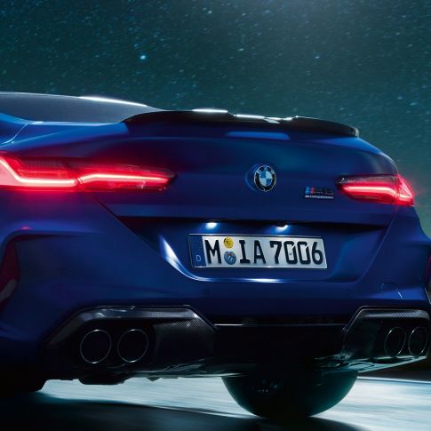 Диффузор М из черного карбона. BMW M8 Competition Coupé в Marina Bay Blue металлик, задняя часть крупным планом ночью с диффузором M из черного карбона.