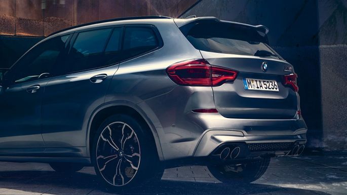 BMW X3 M, боковой вид сзади. BMW X3 M Competition в Donington Grey металлик, экстерьер, боковой вид сзади с двумя людьми на переднем плане.