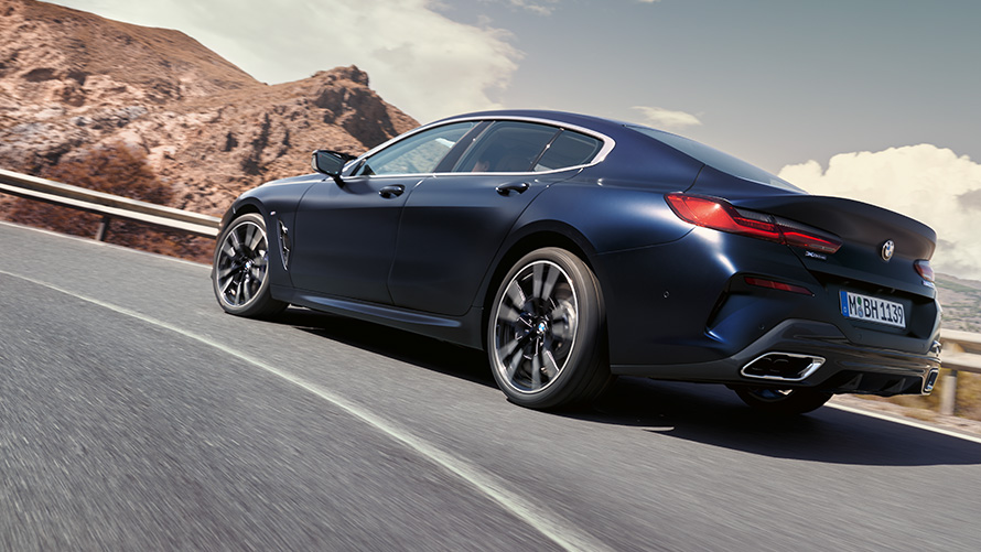 BMW 840i xDrive Gran Coupé G16 LCI Facelift 2022 в движении по горной местности BMW 840i xDrive Gran Coupé G16 LCI Facelift (рестайлинг 2022 года), цвет Синий Портимау металлик, вид сзади с поворотом в три четверти, в движении по горной дороге