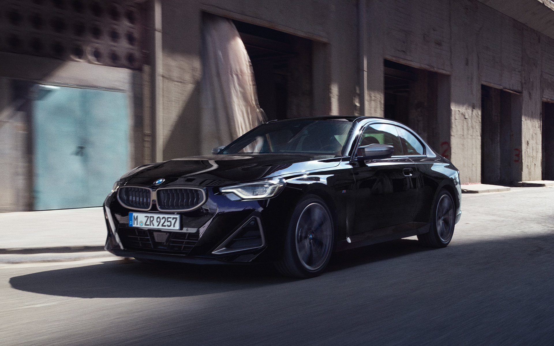 BMW M240i xDrive Coupe G42 2021 &quot;Черный Сапфир металлик&quot;, вид сбоку в три четверти в движении перед зданиями