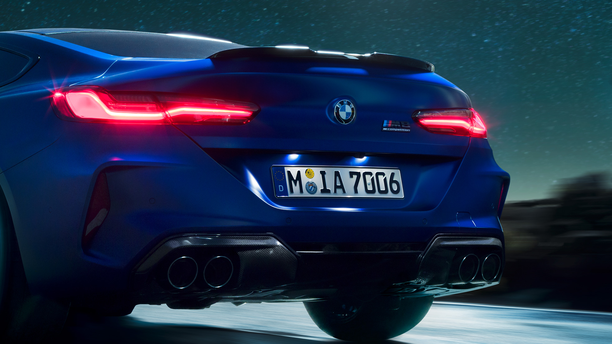 Диффузор М из черного карбона. BMW M8 Competition Coupé в Marina Bay Blue металлик, задняя часть крупным планом ночью с диффузором M из черного карбона.