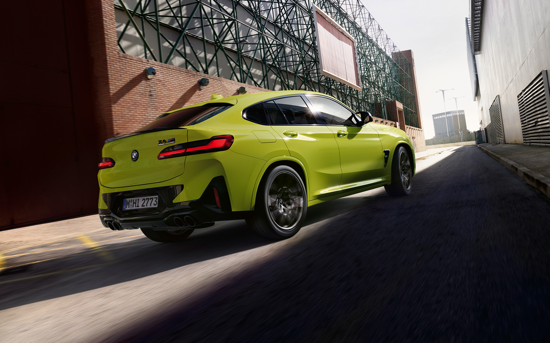 BMW X4 M Competition F98 LCI Facelift 2021 в цвете Sao Paulo Yellow, вид спереди в три четверти проезжая между фабричными зданиями