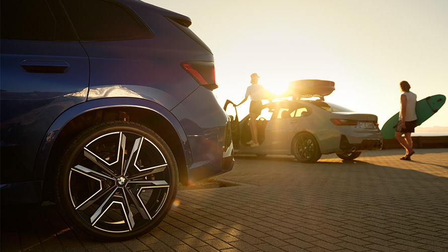 Услуги шиномонтажа BMW Услуги шиномонтажа BMW, два человека на автомобиле BMW X1 U11 на фоне солнца